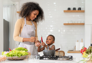 Wall Mural - Multiracial mother and son have fun cooking meal together in kitchen at home. Young multiethnic woman and her little child preparing healthy lunch with fresh vegetable. Happy motherhood lifestyle.