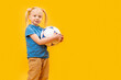 © somemeans - Studio shot of young blonde girl holding soccer ball against yellow background. Child and football. Copy space, mockup