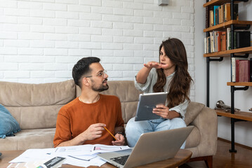 Young smart couple business owners and partners architectural exterior interior designers working from home on laptop computer with blueprint and colors for new client on decoration his new apartment