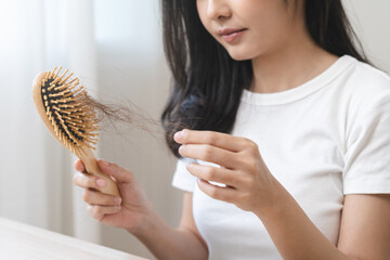 Serious asian young woman holding brush holding comb, hairbrush with fall black hair from scalp after brushing, looking on hand worry about balding. Health care, beauty treatment, hair loss problem.