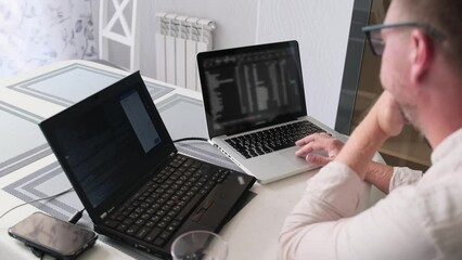 Focused man working by typing on keyboard and look at monitor, programmer work in light office. Professional caucasian male software engineer working remotely.