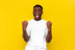 african american man in white t-shirt celebrates victory and raises his hands up on yellow isolated background