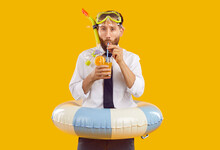 Funny Office Worker Enjoying Summer Holiday. Portrait Of Man In Office Shirt, Tie Snorkeling Mask And Beach Ring Standing Isolated In Yellow Background, Holding Glass And Drinking Tropical Cocktail