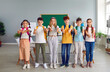 © Studio Romantic - Team of joyful preteen schoolchildren in classroom show thumbs up showing their approval. Boys and girls stand in row with arms outstretched and show ok sign and smile at camera.