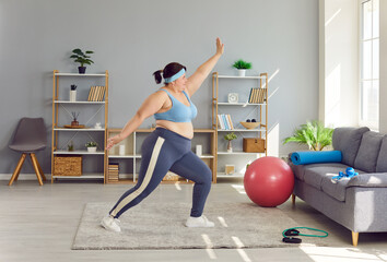 Full length portrait of a funny young fat overweight woman wearing sportswear doing fit warming up exercises in the living room at home. Healthy lifestyle, obesity and workout sport concept.