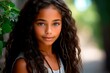 © Zireael - Close-up portrait of a teenage Latino girl with long curly hair on a background of greenery. AI generation