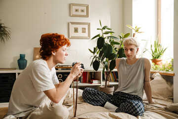 Young man taking pictures of his boyfriend while sitting on bed at home