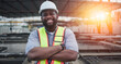 © otello-stpdc - Portrait of Male black civil engineer, contractor, foreman or worker construction in uniform wearing helmet safety standing on construction site. Posing with arms crossed look at camera and smile.