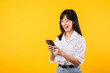 © Jirawatfoto - Portrait beautiful young asian woman happy smile wearing white shirt and denim plants using smartphone isolated on yellow studio background. reading news from smartphone concept.