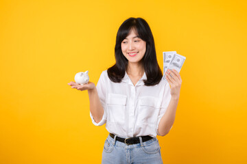 Poster - Portrait beautiful young business asian woman wearing white shirt and denim jean with a lot of cash money and piggy bank isolated on yellow background. Wealth money saving, finance investment concept.