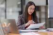 © David - Asian business woman wear glasses or accountant working on calculator to calculate business data, accounting document and laptop computer at office, business concept