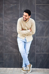 Wall Mural - Cheerful young arabic guy standing against black wall with arms crossed