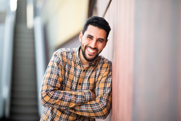 Wall Mural - Smiling young arabic guy with arms crossed standing against a wall