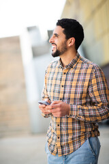 Wall Mural - Smiling middle eastern man walking outside with cell phone