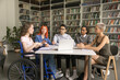 Multiethnic team of students inclusively classmate girl with disability studying together in campus, sitting at table in library, talking, discussing education, class project, brainstorming