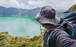 © ADDICTIVE STOCK - Anonymous male hiker in hat with backpack looking away while making photo and standing on hill against Quilotoa lagoon Ecuador