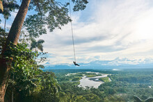 Man Swinging In Tropical Valley With Green Trees