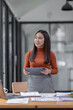 © David - Young business entrepreneur Asian woman wear glasses using tablet , standing near the window in workplace business finance concept.