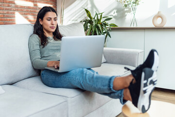 Wall Mural - Beautiful young woman working with her laptop while sitting on a couch at home.