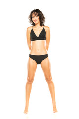 Wall Mural - Young smiling exotic brunette woman in black bikini swimsuit posing on a white background. Front view.