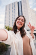 © Jose Calsina - Vertical portrait of pretty young adult woman with thooty smile having fun taking a selfie using a social media. Happy teenage female laughing and looking at camera with cheerful expression outside