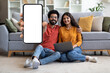 © Prostock-studio - Great App. Cheerful Indian Spouses Demonstrating Blank Smartphone At Home