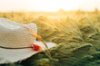 Rustic straw hat and red poppy on barley ears in evening field close up. Wildflowers and farm hat in summer countryside. Atmospheric moment in evening meadow