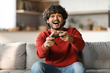 Wall Mural - Young happy indian man laughing and playing video games on weekend