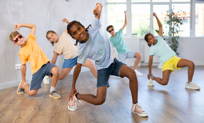 Positive juvenile boy engaged in Breakdancing together with children's group in training room during workout session