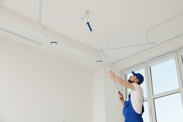 Poster - Worker in uniform painting ceiling with roller indoors. Space for text