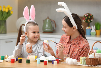 Canvas Print - Mother and her cute daughter painting Easter eggs at table in kitchen