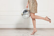 © New Africa - Woman in high heeled shoes and golden dress with disco ball near white wall indoors, closeup