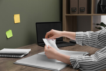 Wall Mural - Woman putting paper sheet into punched pocket at wooden table, closeup