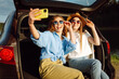 © maxbelchenko - Smiling young womans have fun in the back seat of a car while traveling. Girlfriends take selfies, laugh and relax while sitting in car and enjoying the sunny weather. Active lifestyle.