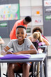 Vertical portrait of smiling african american schoolboy in wheelchair at desk in class, copy space