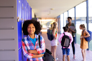 Sticker - Portrait of smiling biracial school girl leaning on lockers in school corridor with copy space