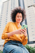 © Jose Calsina - Young adult happy hispanic woman watching funny videos on a smartphone social media app. Latin cheerful female using a cellphone to browse on internet. Girl sending messages with mobile phone outside