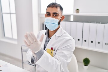 Wall Mural - Young hispanic man doctor wearing medical mask wearing gloves at clinic