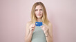 © Krakenimages.com - Young blonde woman holding credit card with serious face over isolated pink background