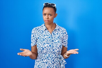 Wall Mural - African american woman standing over blue background clueless and confused with open arms, no idea concept.