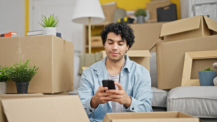 Poster - Young latin man using smartphone sitting on floor at new home