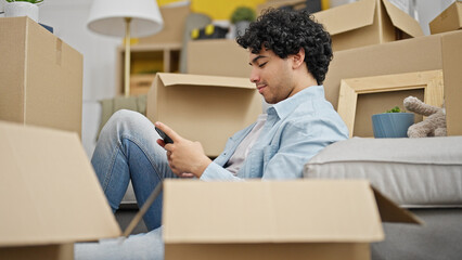 Poster - Young latin man using smartphone sitting on floor at new home