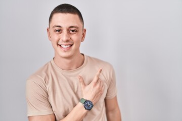 Wall Mural - Young man standing over isolated background cheerful with a smile on face pointing with hand and finger up to the side with happy and natural expression