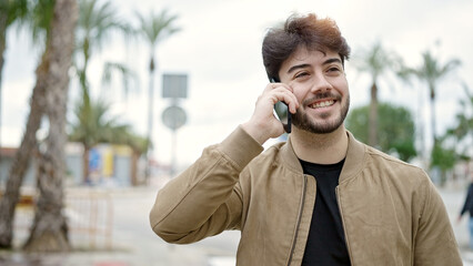 Wall Mural - Young hispanic man talking on smartphone smiling at street