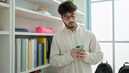 Wall Mural - Young hispanic man student using smartphone at library university