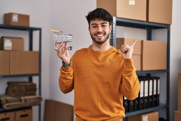 Sticker - Hispanic man with beard standing by manikin at small business holding cart smiling happy pointing with hand and finger to the side