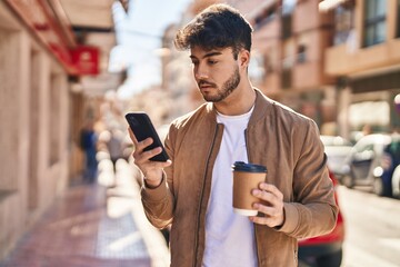 Wall Mural - Young hispanic man using smartphone drinking coffee at street