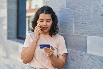 Young woman talking on the smartphone and using credit card at street