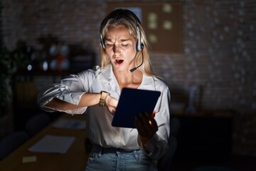 Sticker - Young blonde woman working at the office at night looking at the watch time worried, afraid of getting late