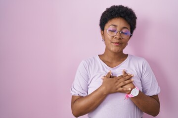 Canvas Print - Young african american woman standing over pink background smiling with hands on chest with closed eyes and grateful gesture on face. health concept.